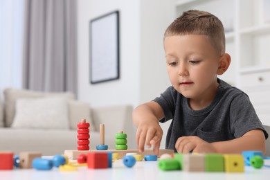 Photo of Motor skills development. Little boy playing with stacking and counting game at table indoors