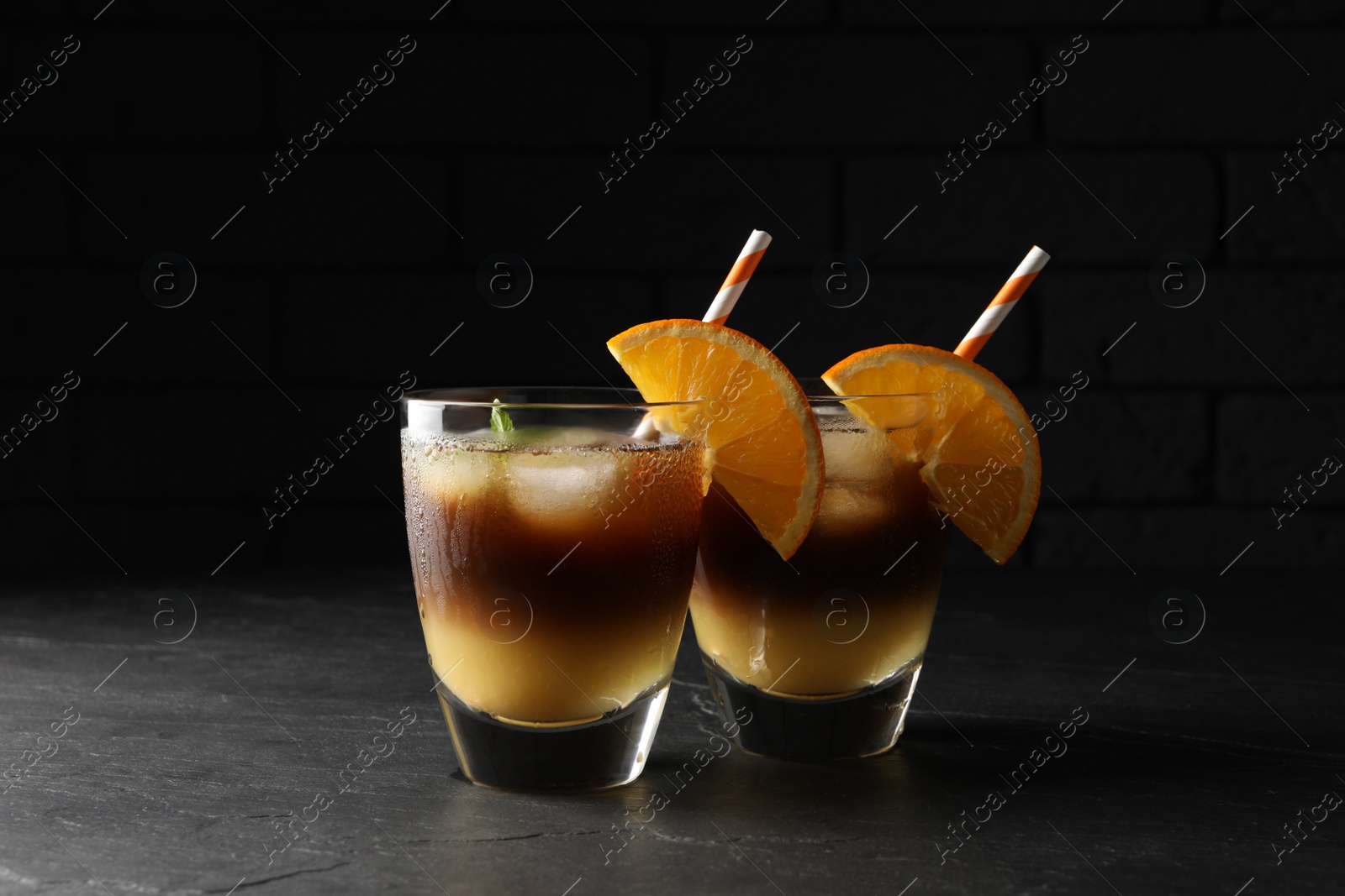 Photo of Tasty refreshing drink with coffee and orange juice on grey table against dark background