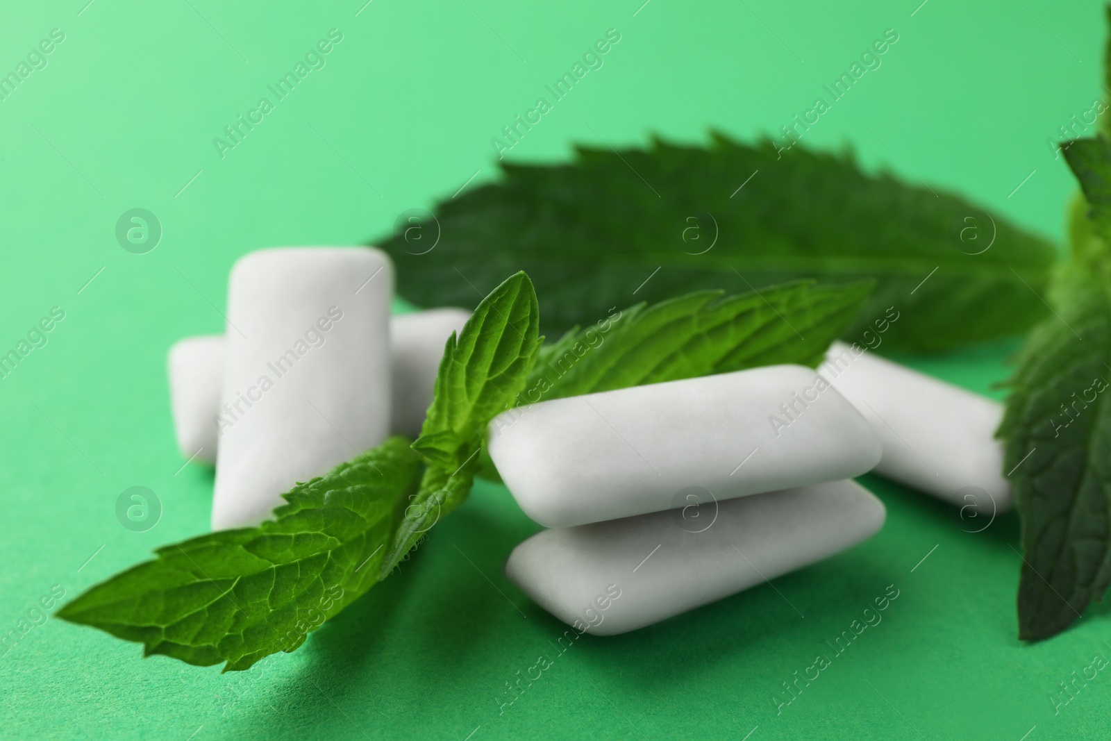 Photo of Tasty white chewing gums and mint leaves on green background, closeup