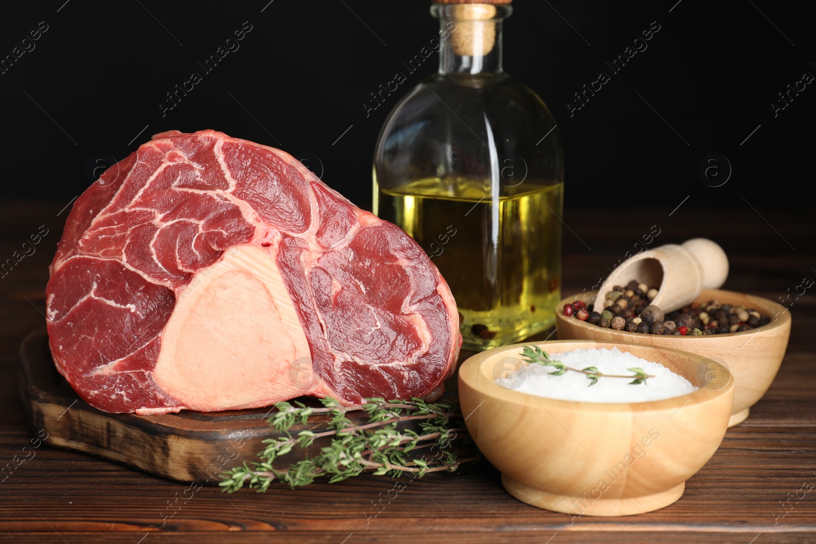 Photo of Piece of raw beef meat, thyme, oil and spices on wooden table against black background, closeup