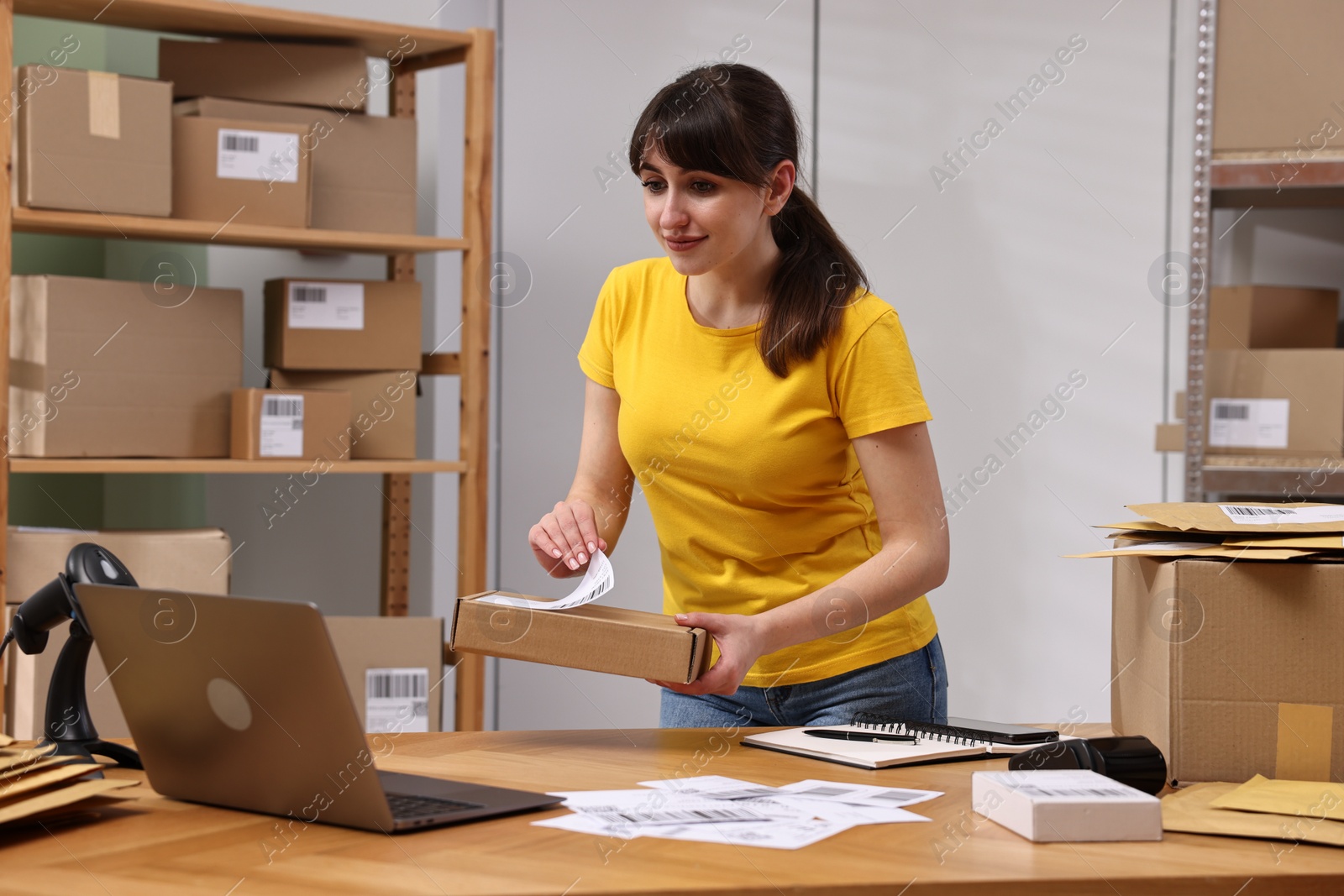 Photo of Parcel packing. Post office worker sticking barcode on box at wooden table indoors