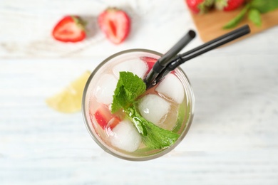 Glass of refreshing drink with strawberry and lime on white table, top view
