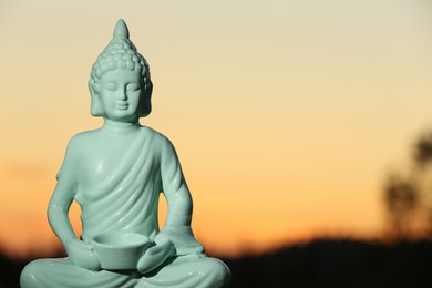 Photo of Decorative Buddha statue outdoors at sunset. Space for text