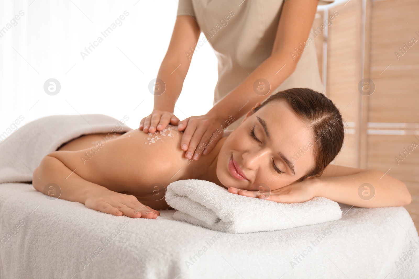 Photo of Young woman having body scrubbing procedure with sea salt in spa salon