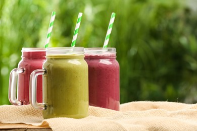 Different delicious smoothies in mason jars on table against blurred background, space for text