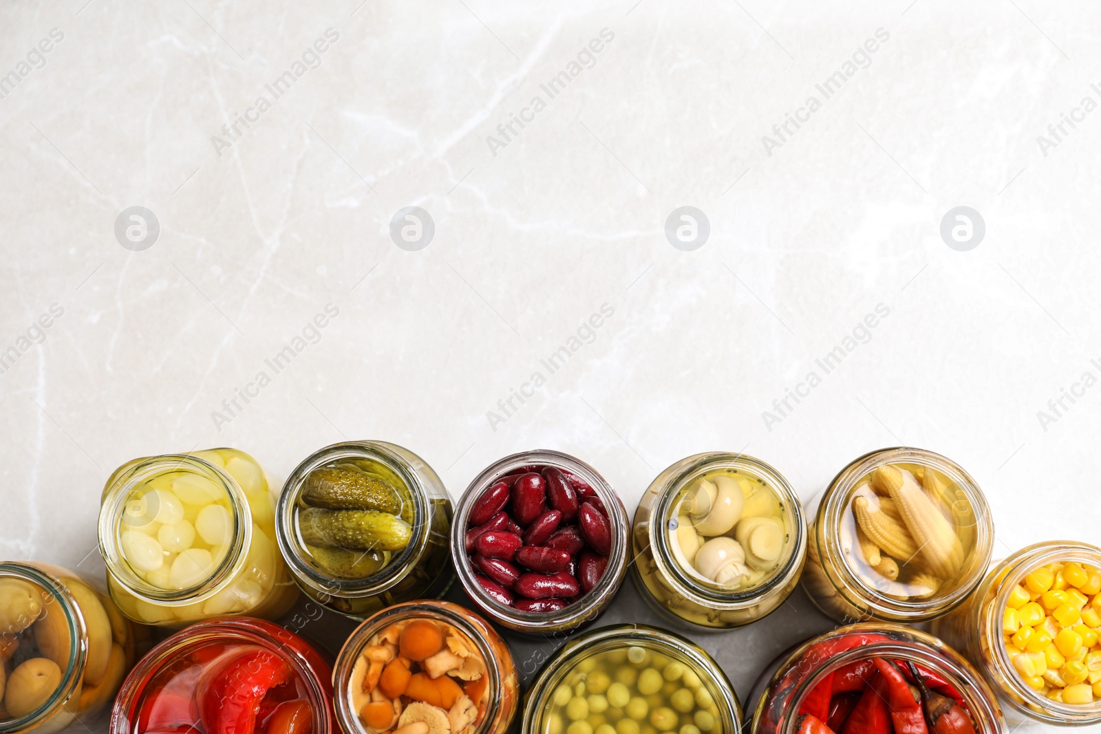 Photo of Glass jars with different pickled vegetables on light grey marble table, flat lay. Space for text