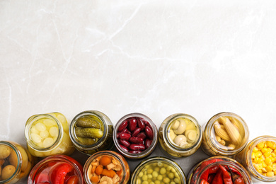 Glass jars with different pickled vegetables on light grey marble table, flat lay. Space for text