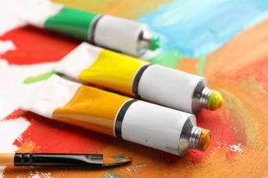 Photo of Tubes of colorful oil paints and brush on canvas with abstract painting, closeup