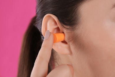Photo of Young woman inserting foam ear plug on pink background, closeup
