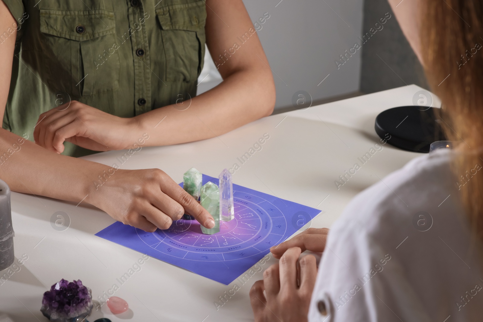 Photo of Astrologer predicting client's future with zodiac wheel and crystals at table indoors, closeup