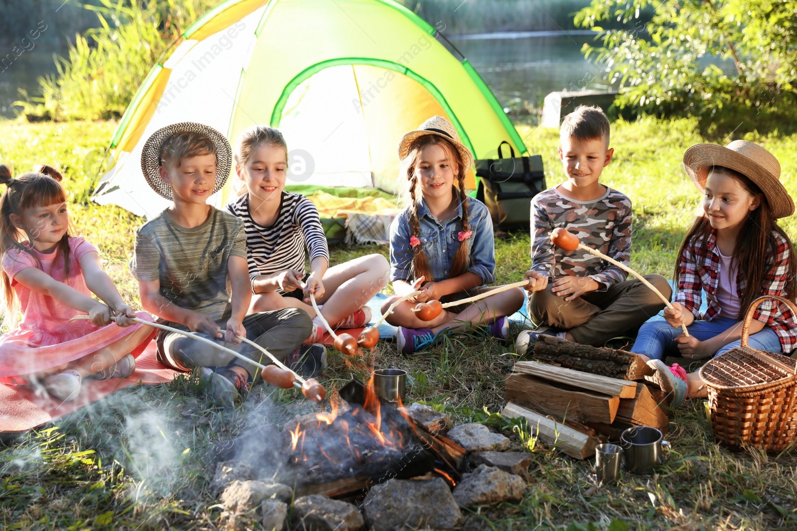 Photo of Little children frying sausages on bonfire. Summer camp