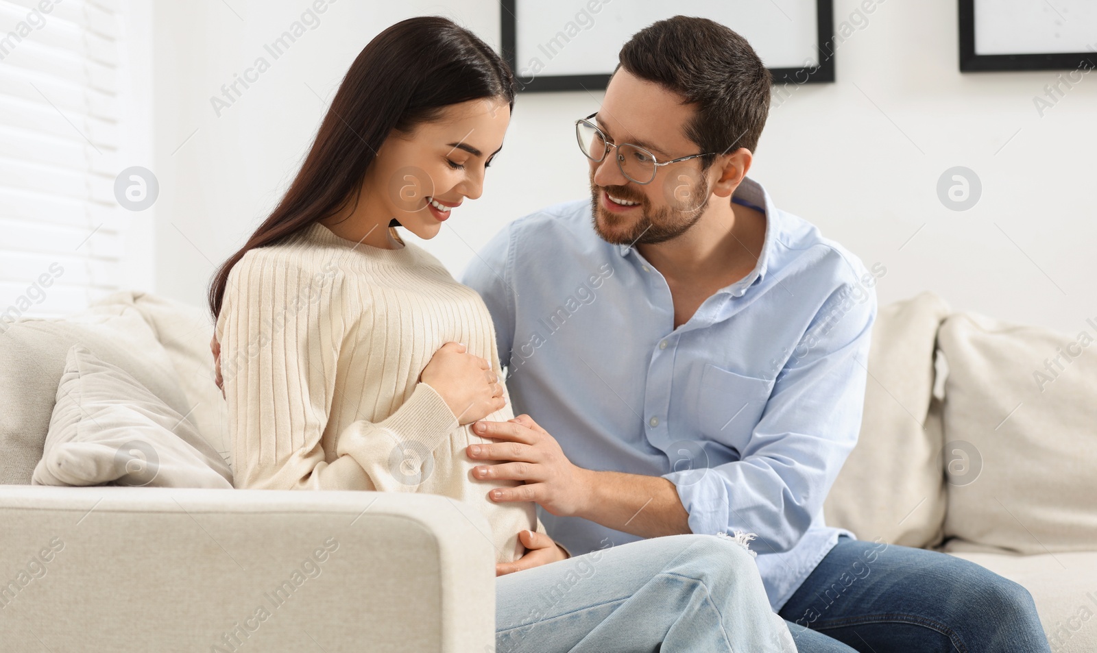 Photo of Happy pregnant woman spending time with her husband on sofa at home