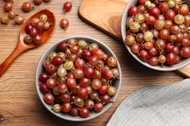 Photo of Bowls full of ripe gooseberries on wooden table, flat lay