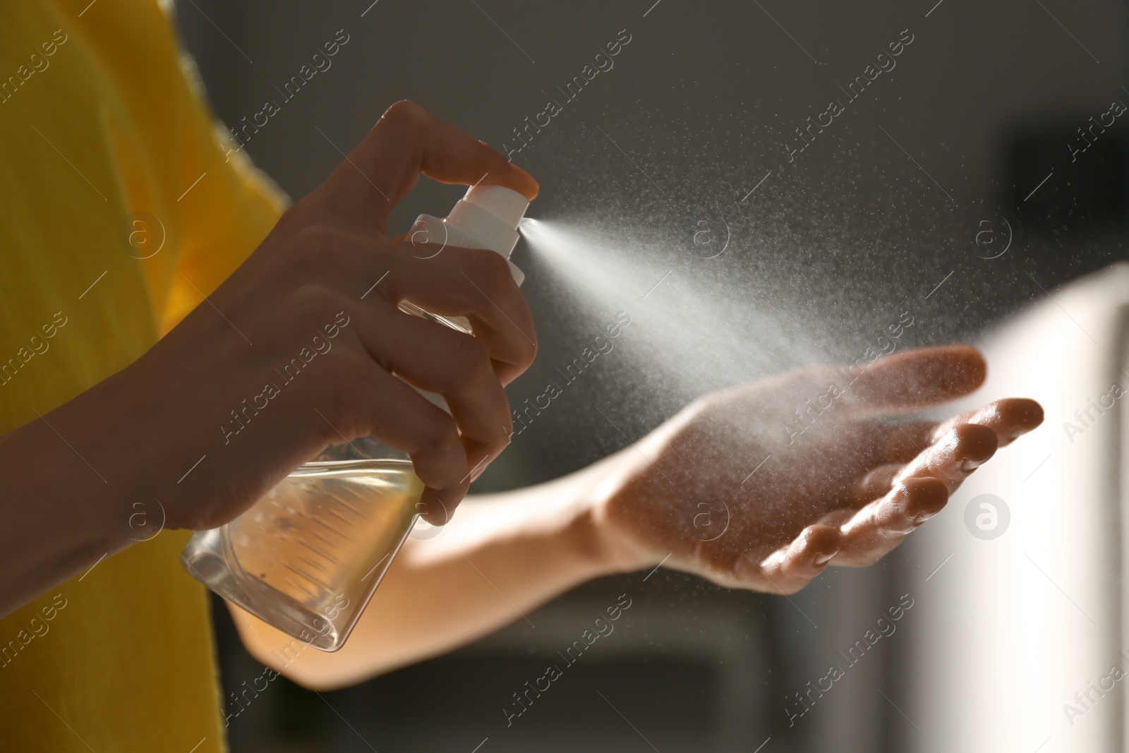 Photo of Little girl spraying antiseptic onto hand indoors, closeup