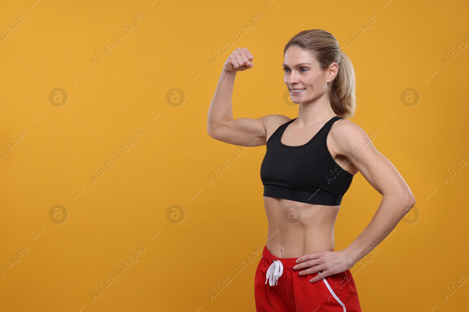 Photo of Portrait of sportswoman showing muscles on yellow background, space for text