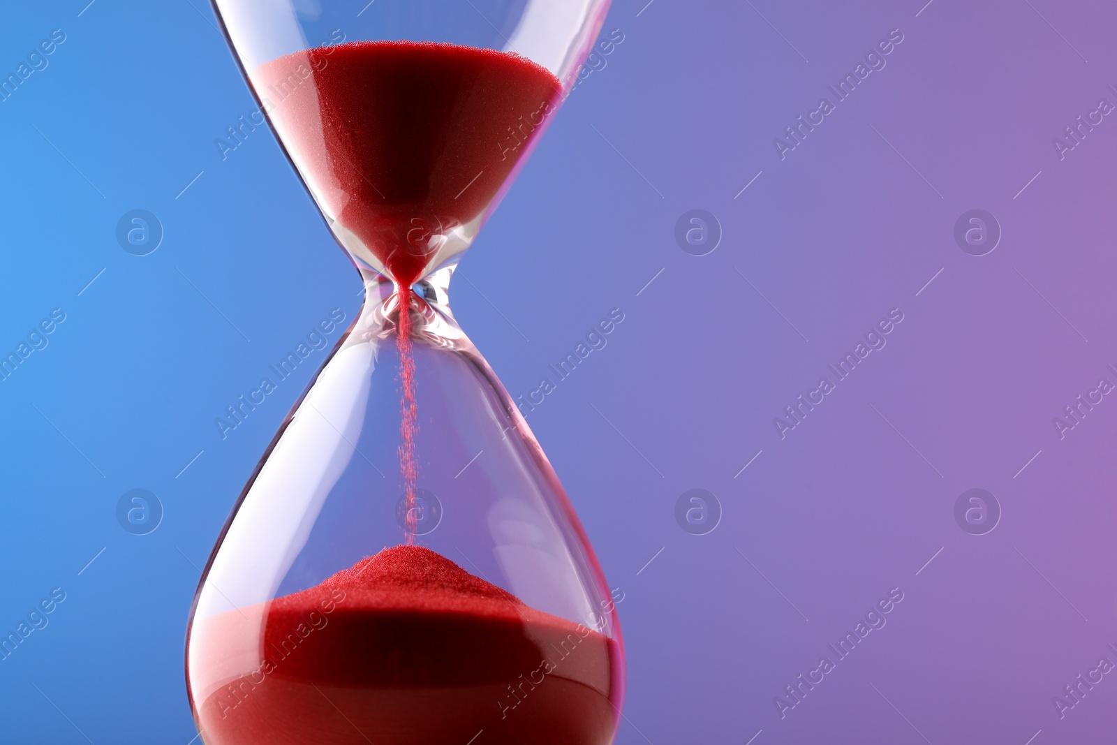 Photo of Hourglass with flowing red sand on color background. Space for text