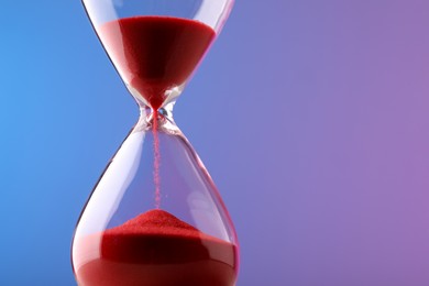 Hourglass with flowing red sand on color background. Space for text