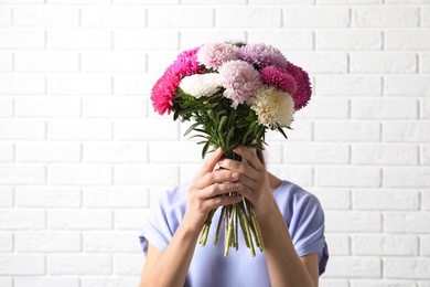 Photo of Woman holding beautiful aster flower bouquet against brick wall