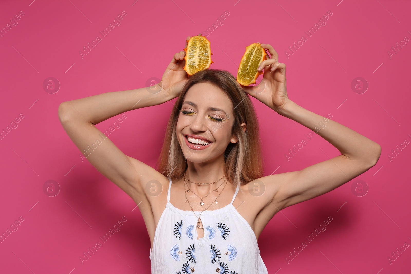 Photo of Young woman with fresh kiwano on pink background. Exotic fruit