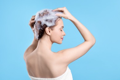 Young woman washing her hair with shampoo on light blue background