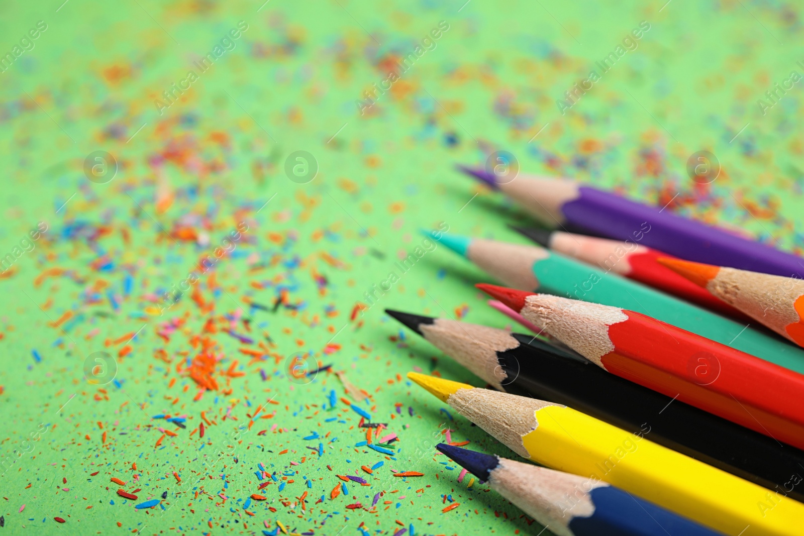 Photo of Color pencils and shavings on green background, closeup
