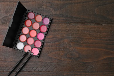 Photo of Colorful lipstick palette and brushes on wooden table, flat lay with space for text. Professional cosmetics