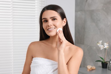 Young woman cleaning her face with cotton pad in bathroom