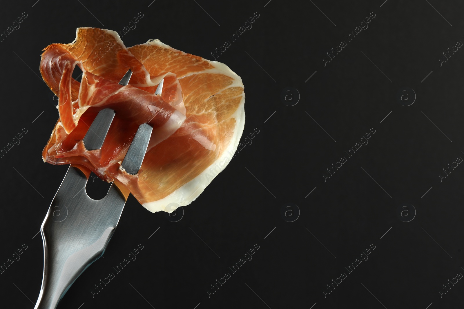 Photo of Fork with slice of tasty jamon on black background, closeup. Space for text