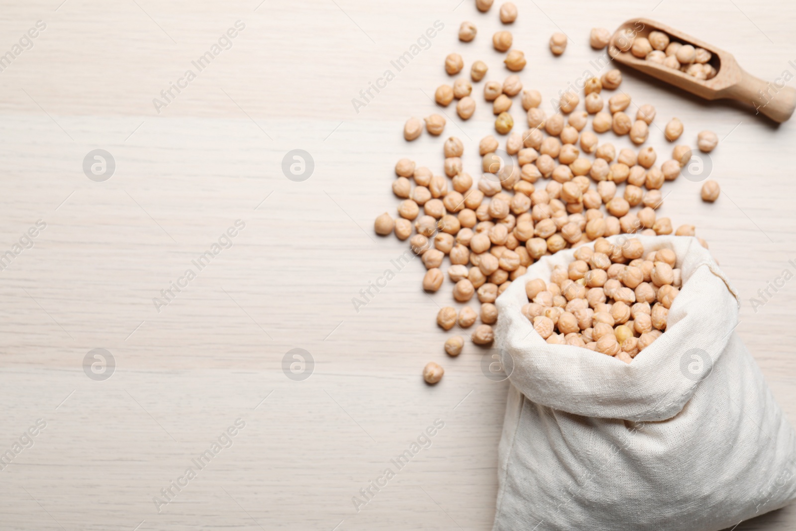 Photo of Sack and scoop with chickpeas on wooden table, flat lay. Space for text