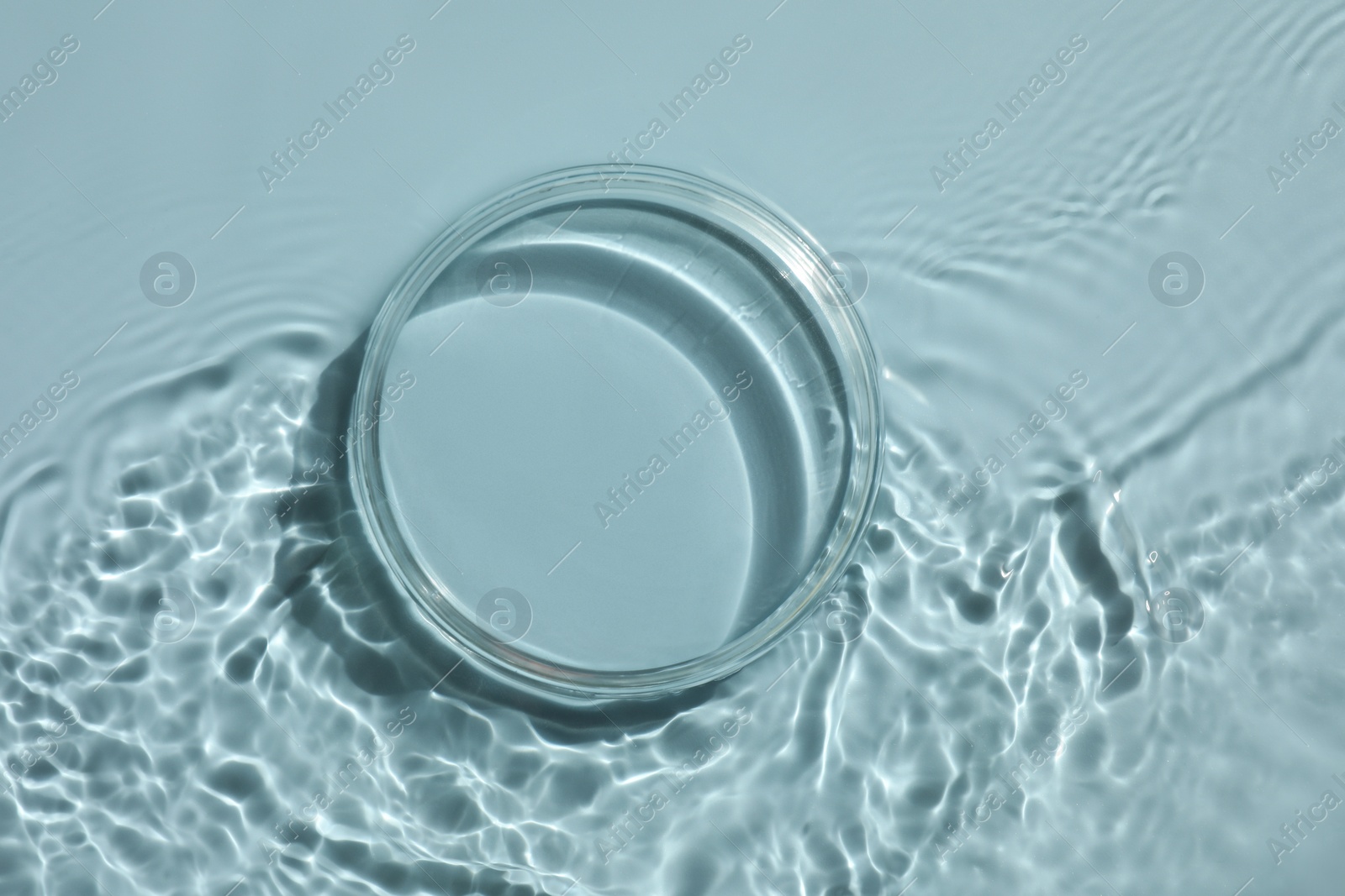 Photo of Stylish presentation for product. Glass podium in water on light blue background, top view