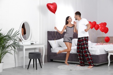 Young couple dancing in bedroom decorated with air balloons. Celebration of Saint Valentine's Day