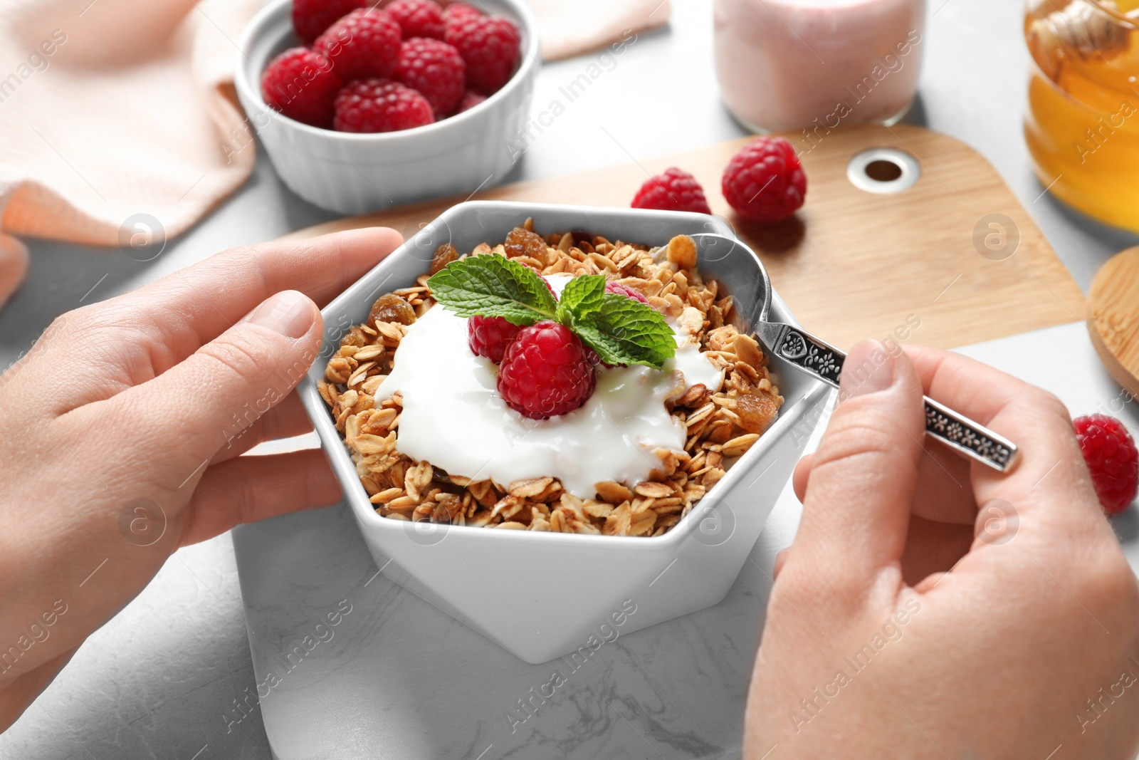 Photo of Woman eating delicious yogurt with granola and raspberries at table, closeup