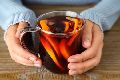 Photo of Woman holding glass cup of tasty mulled wine at wooden table, closeup