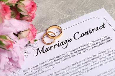 Marriage contract, golden wedding rings and flowers on grey table, closeup