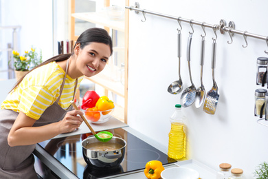 Young woman cooking tasty soup in kitchen