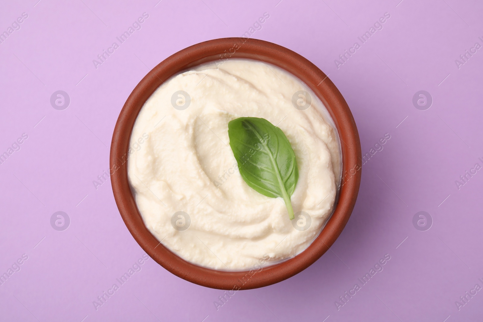 Photo of Delicious tofu sauce and basil leaf in bowl on violet background, top view