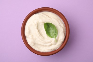 Photo of Delicious tofu sauce and basil leaf in bowl on violet background, top view