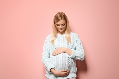 Beautiful pregnant woman in sweater on color background