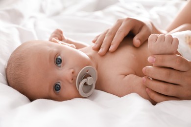 Photo of Mother and her cute little baby with pacifier on bed, closeup