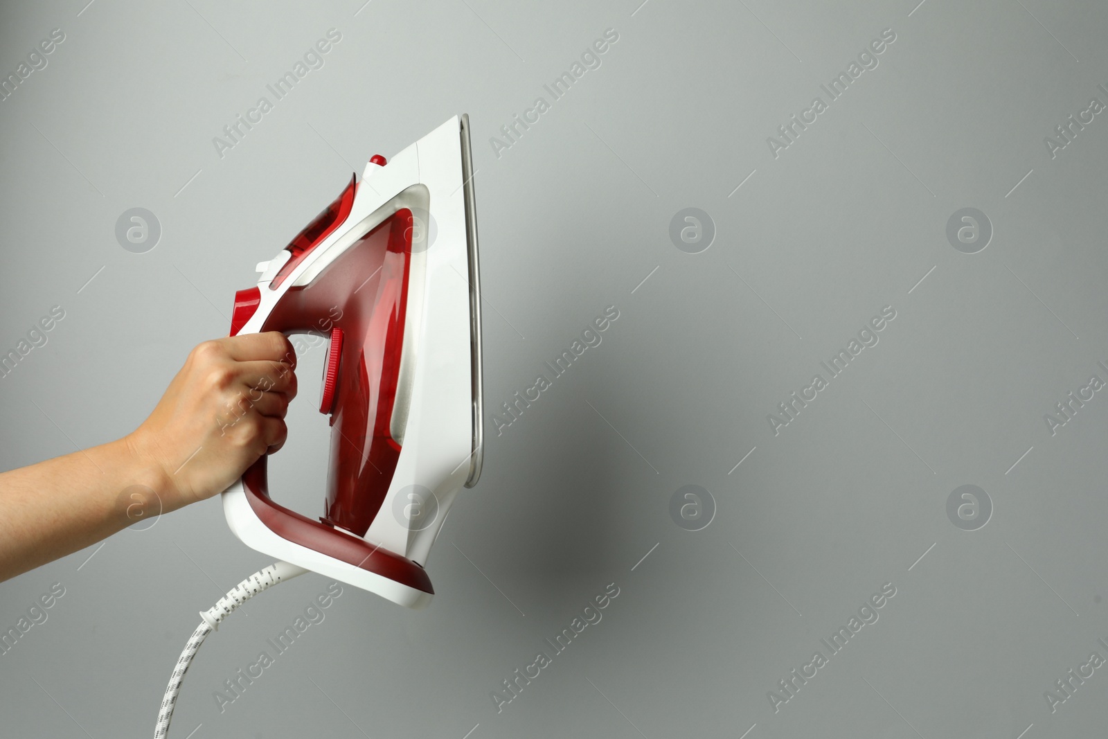 Photo of Woman holding modern iron on light grey background, closeup. Space for text