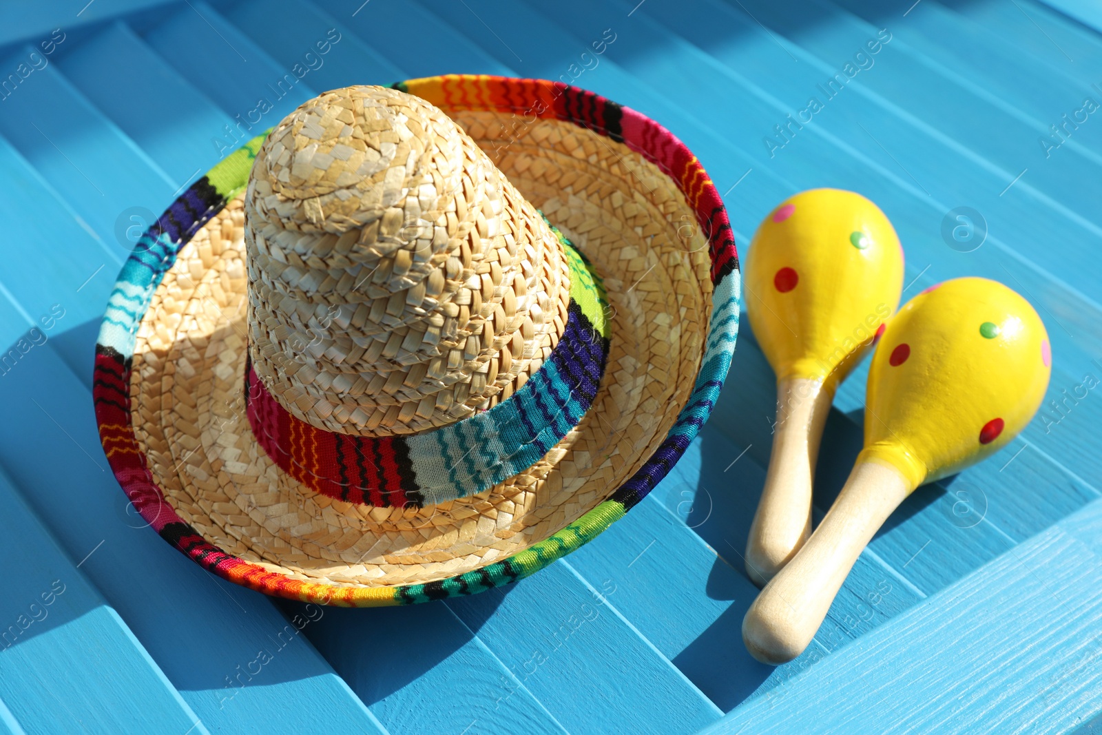 Photo of Mexican sombrero hat and maracas on blue wooden surface