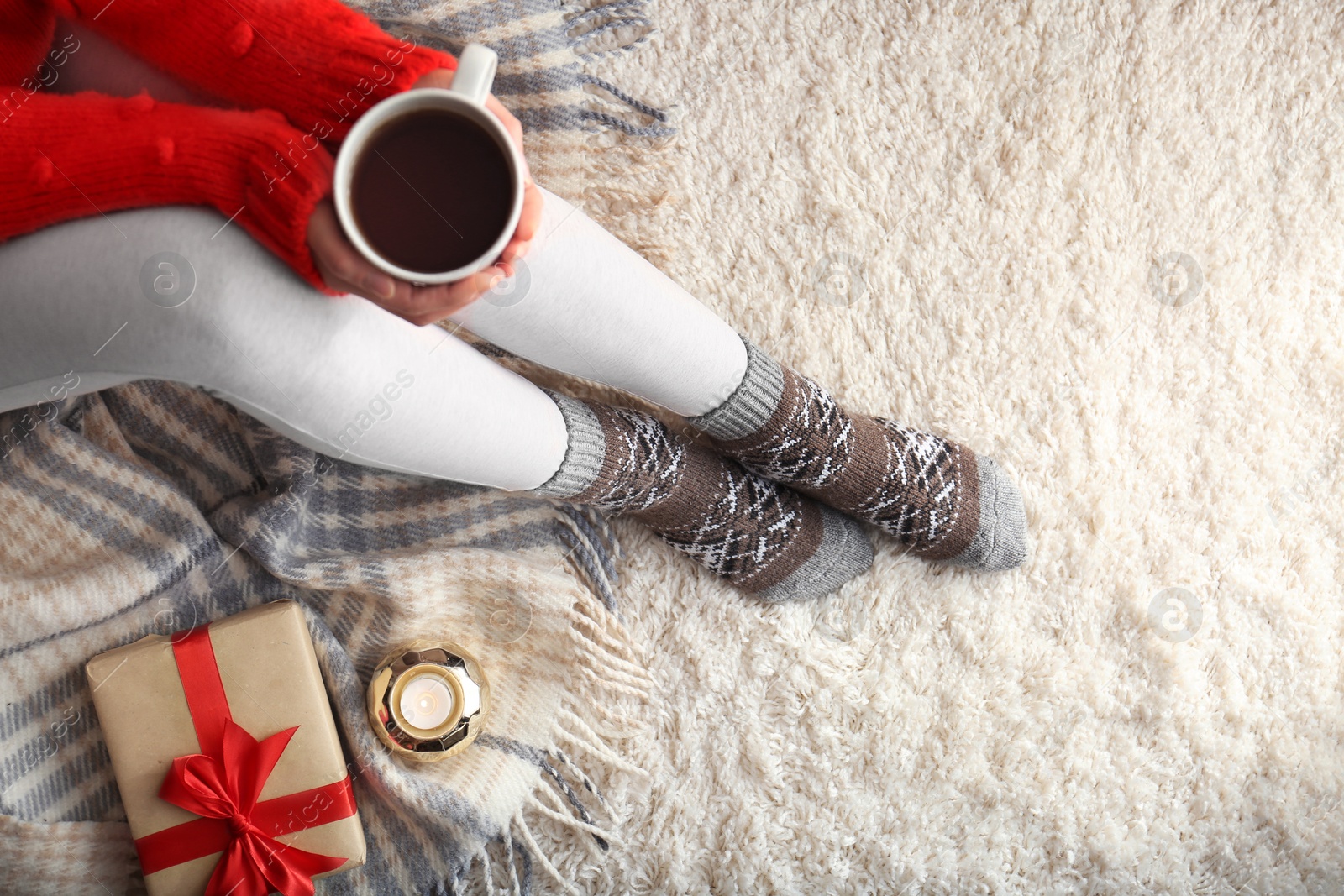 Photo of Woman wearing knitted socks on rug, top view. Warm clothes