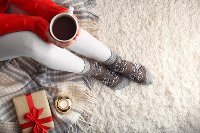 Woman wearing knitted socks on rug, top view. Warm clothes