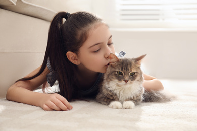 Cute little girl with cat lying on carpet at home. First pet