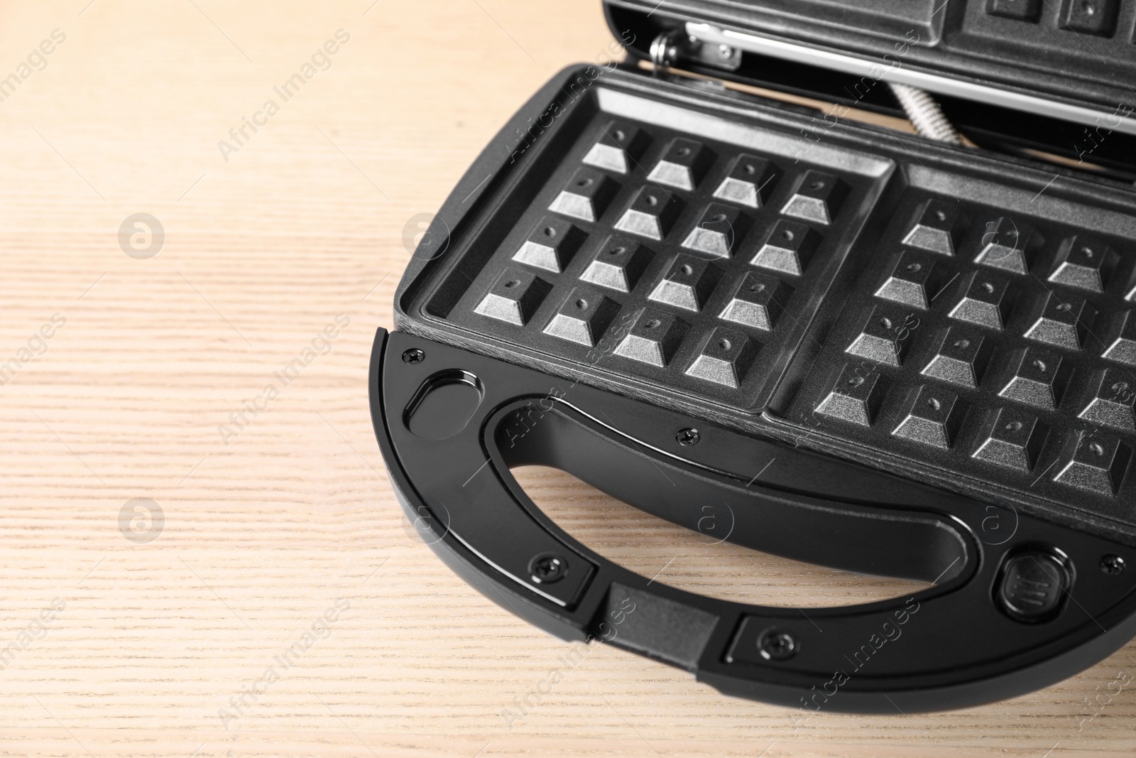 Photo of Modern waffle iron on wooden table, closeup