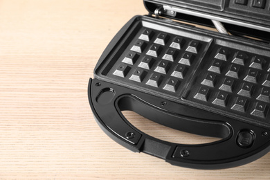 Photo of Modern waffle iron on wooden table, closeup