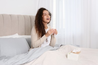 Sick African American woman with box of tissues in bed at home