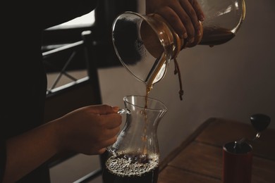 Barista pouring coffee into glass jug in cafe, closeup