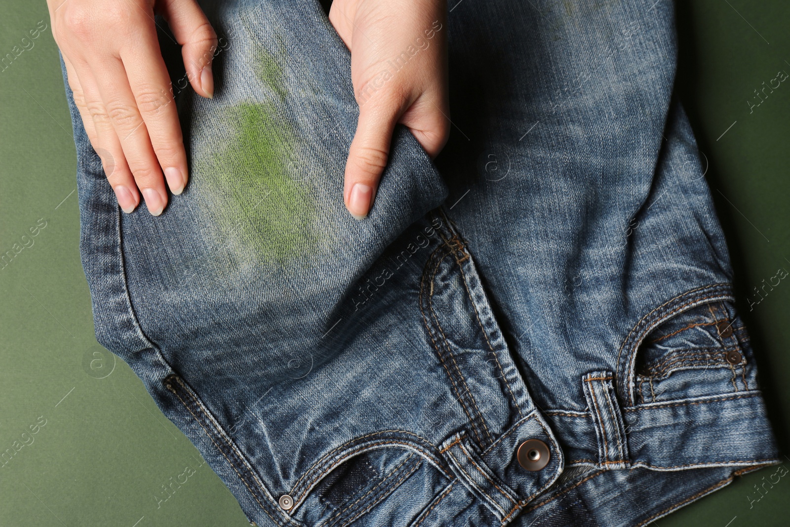 Photo of Woman holding jeans with stain on green background, top view