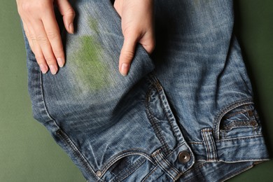 Woman holding jeans with stain on green background, top view